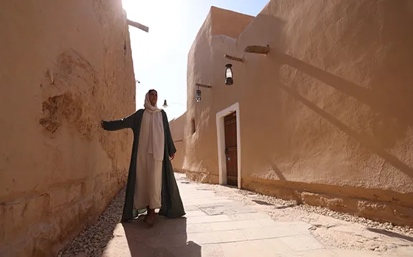 A person in a robe standing in a narrow street Description automatically generated